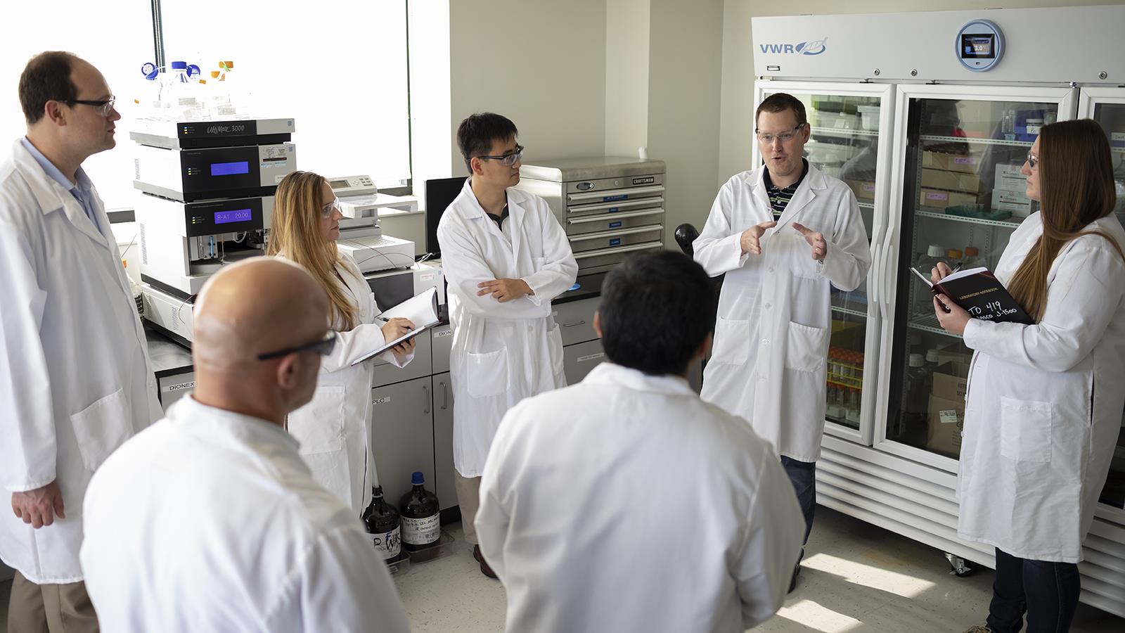 Group of scientists wearing white lab coats having a stand up discussion